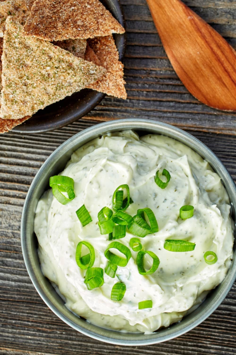 Top View of a Bowl of Blue Cheese Dip with Scallions on a Wooden Table and Plate of Homemade Chips to the Side