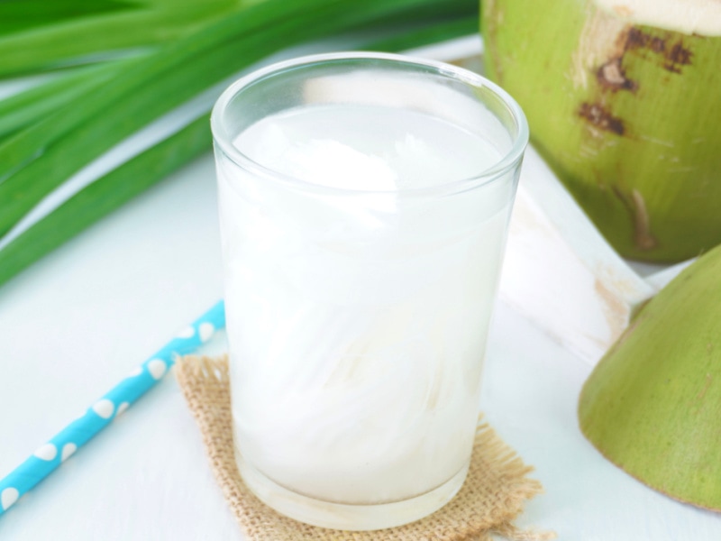 A Glass of Coconut Water and Coconuts on a Wooden Table