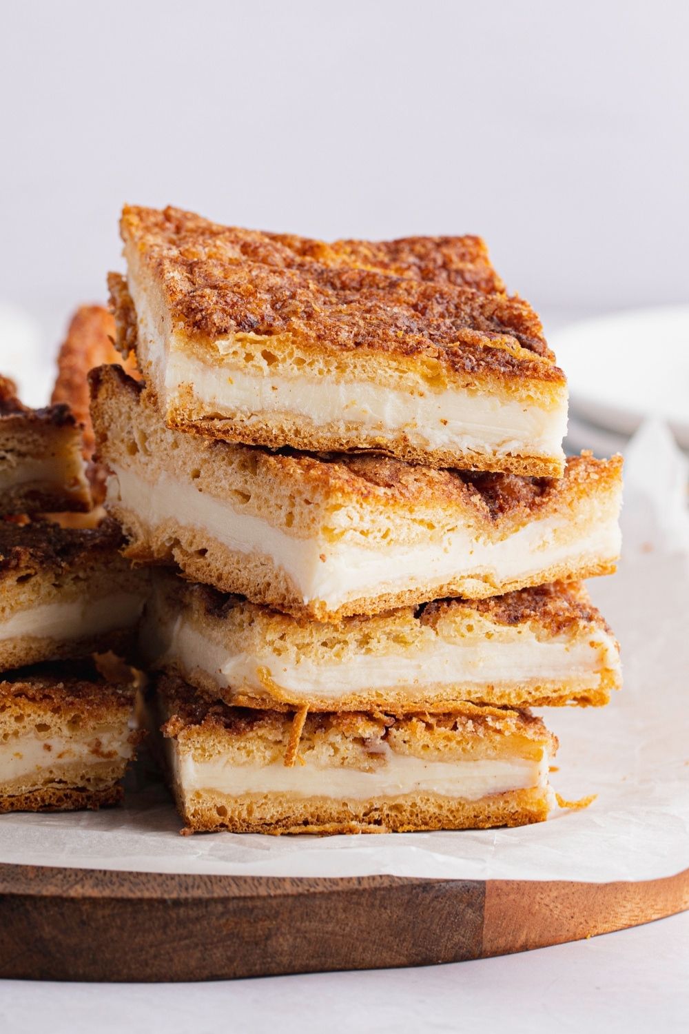 Close-up of a Stack of Creamy Sopapilla Cheesecake Bars on Parchment Paper on a Wooden Cutting Board