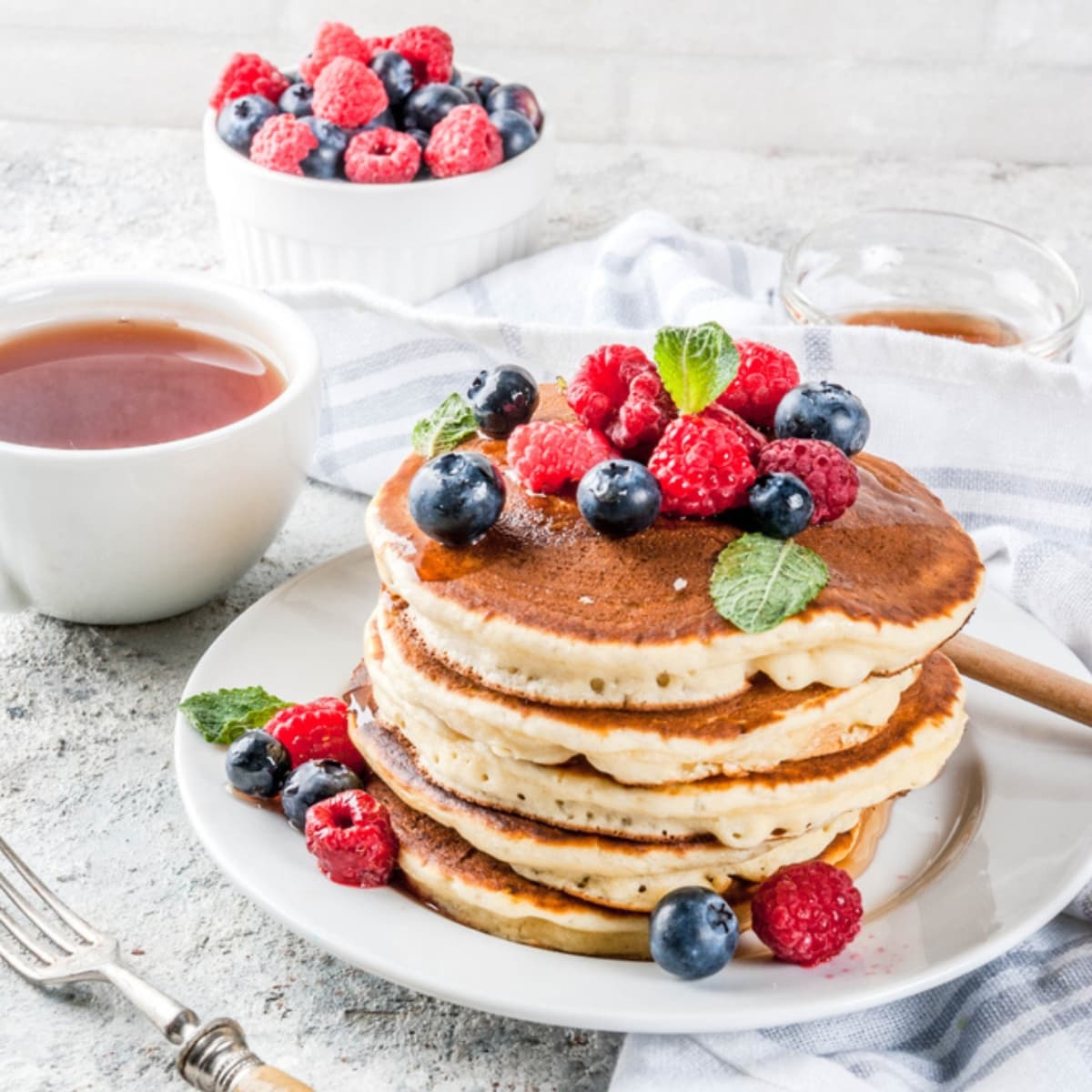 Homemade Oat Flour Pancakes with Fresh Berries and Mint Served on a Plate, Dish of Syrup on the Side